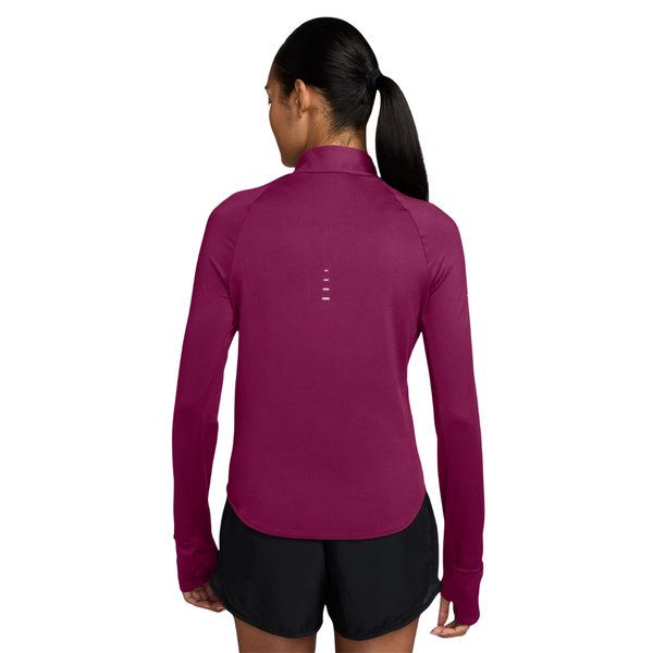 En mørkrosa Nike Swift Half Zip-løbetrøje til kvinder i farven True Berry/Reflective Silver med reflekterende detaljer på ryggen, båret over sorte sportsshorts.