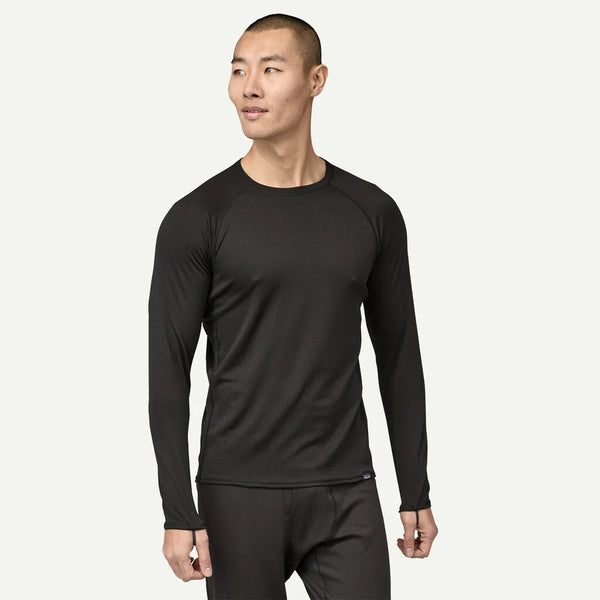 En person er iført Patagonia Cap MW Crew, Herre, Black langærmet top og matchende sorte bukser og vender lidt til venstre mod en almindelig lys baggrund.