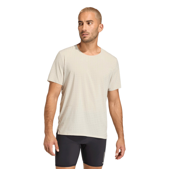 En mand med kort blondt hår bærer Adidas Adi365 Hk Tee, Herre, Putgre - en lys beige træningstop til mænd lavet af åndbart materiale - og sorte shorts. Han står let drejet med afslappede arme mod en almindelig hvid baggrund.