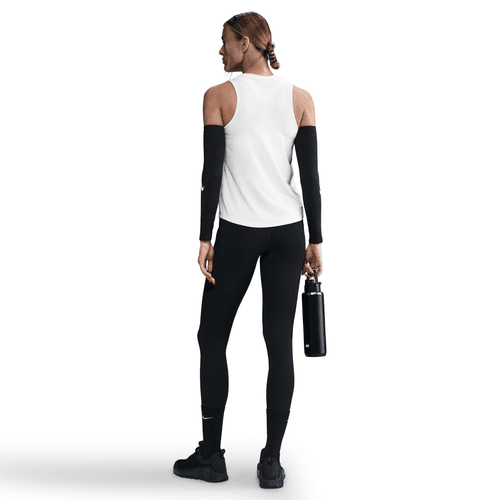En kvinde i Nike Dri-FIT Classic Tank Top, Dame, White/Black, sorte leggings, ærmer og sneakers står med ryggen til og holder en sort vandflaske. Baggrunden er helt hvid.