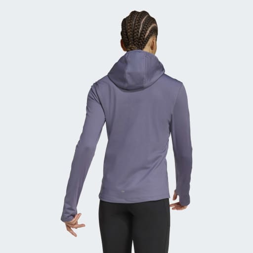 En kvinde med flettet hår ses bagfra iført en langærmet lyslilla Adidas Otr Bin Hz, Dame, Previo-top og sorte bukser på en ensfarvet baggrund.