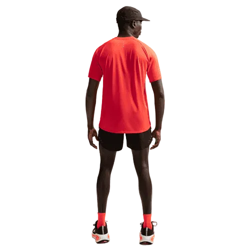 En person står med ryggen til og er iført en fugttransporterende rød kortærmet trøje, Stride 5" Brief-Lined Running Shorts fra Nike i Black/Reflective Silv, røde sokker, sorte løbesko med hvide såler og en sort kasket. Baggrunden er ensfarvet og lys.