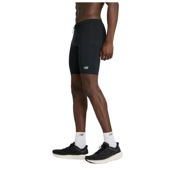 En person bærer NB Sleek Pocket Half Tight 9" (Herre, Black) fra New Balance over fugttransporterende tights, med hvide New Balance-sokker og sorte løbesko. Billedet viser underkroppen fra taljen og ned mod en hvid baggrund.