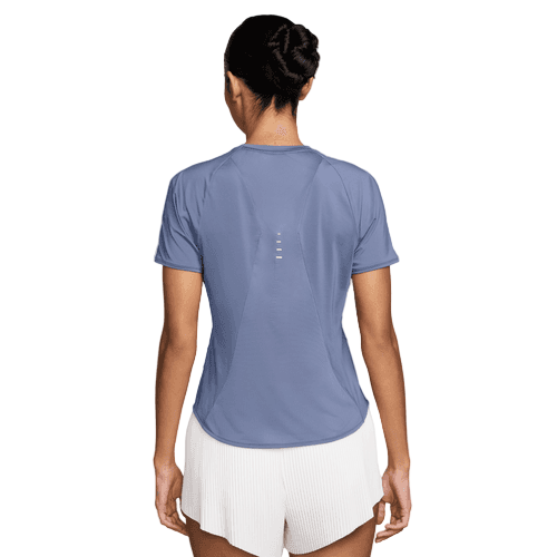 En kvinde kigger væk fra kameraet iført en Nike Swift SS Løbetop til kvinder i World Indigo/Reflective Silver med korte ærmer og refleksdetaljer øverst på ryggen, sammen med hvide shorts.