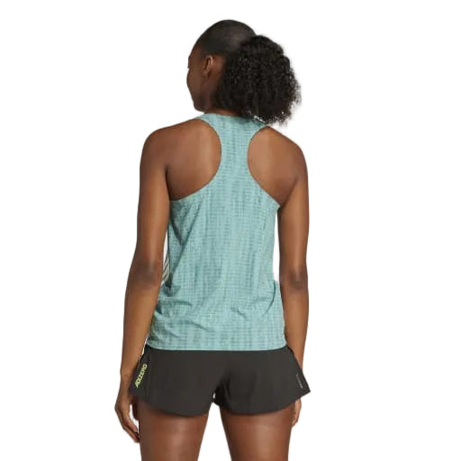 En kvinde står med ryggen til kameraet i en powtea/pretea Adidas Adizero Singlet, Dame og sorte shorts. Hendes krøllede hestehale og den hvide baggrund fremhæver denne ultralette løbetøj.