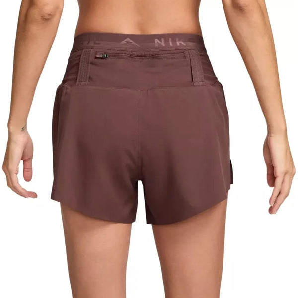 En person ses bagfra iført Nike Dri-FIT Trail Mid-Rise 4" Brief-Lined Running Shorts til kvinder i Red Sepia/Black med en lille lynlåslomme nær linningen. Baggrunden er hvid.