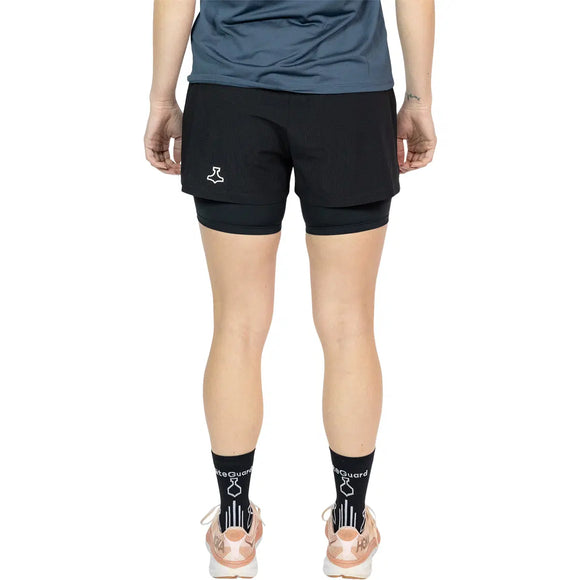 En kvinde ses bagfra iført en blå skjorte, Liiteguard Glu-Tech Running 2In1 Shorts i sort, sorte sokker og lyse sneakers på en almindelig hvid baggrund.