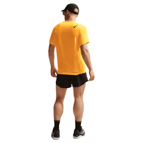 En mand kigger væk, iført sort kasket, sorte shorts, strømper, grå sko og Nike Aeroswift SS Top til mænd i Laser Orange/Black med fugttransporterende materiale. Nike-logoet er synligt på trøjen. Baggrunden er almindelig hvid.