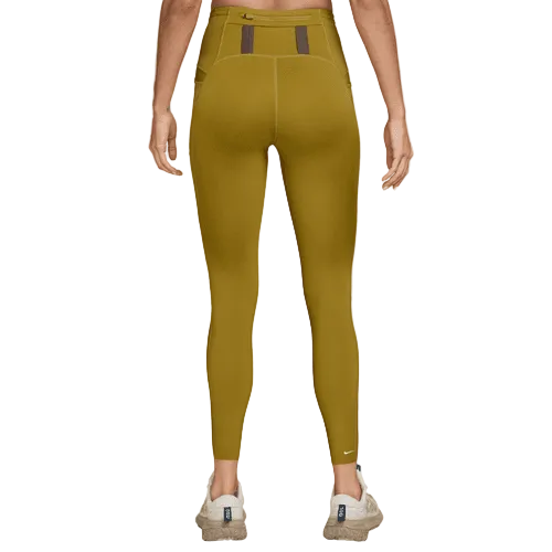 En person kigger væk fra kameraet iført Nike ACG 7/8 Running Tights til kvinder i Peat Moss/Ironstone/Summit White med to brune detaljer i linningen, et lille hvidt logo nær anklen og lyse sneakers.