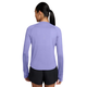 En person med langt, mørkt hår sat op i en lav hestehale står med ryggen til kameraet iført Nike Swift UV langærmet løbetrøje til kvinder i farven Purple Pulse/Reflective Silver og sorte shorts foran en ensfarvet hvid baggrund.