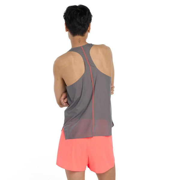 En person med kort sort hår står med armene over kors og kigger væk, iført New Balance Race Day Ultra Light Singlet, Herre, i Urgent Red. De parrer den med lyse koralfarvede shorts mod en almindelig hvid baggrund.