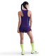 En kvinde med flettet hår står med ryggen til og er iført en ærmeløs Nike AeroSwift Running Singlet i Court Purple/White og matchende shorts, neongrønne knæstrømper og hvide sportssko med tykke såler på en almindelig hvid baggrund.
