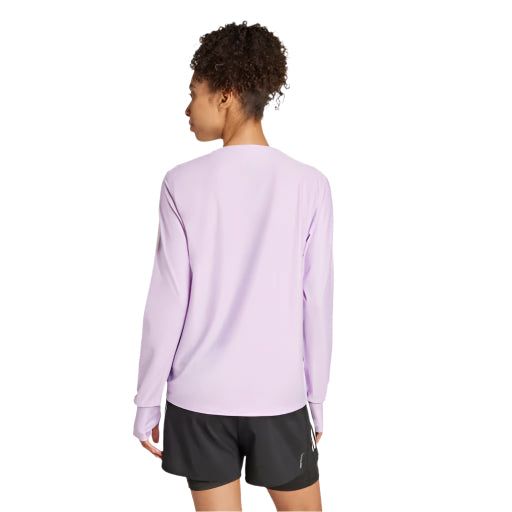 En kvinde med kort krøllet hår ses bagfra iført en Adidas Otr B Ls, Dame, Powplu-top og sorte sportsshorts, stående på en hvid baggrund.