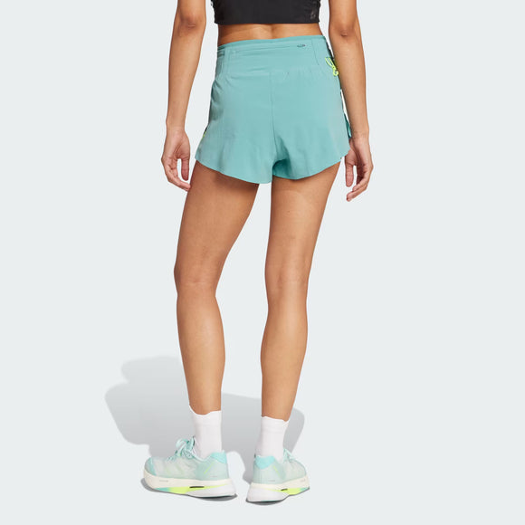 En person står på en lys baggrund, vist bagfra med afslappede arme, iført en sort Adidas-crop top, Adizero Running Gel Pocket Shorts 4" til kvinder i Powder Teal, hvide strømper og lyseblå sneakers med neonfarvede detaljer.