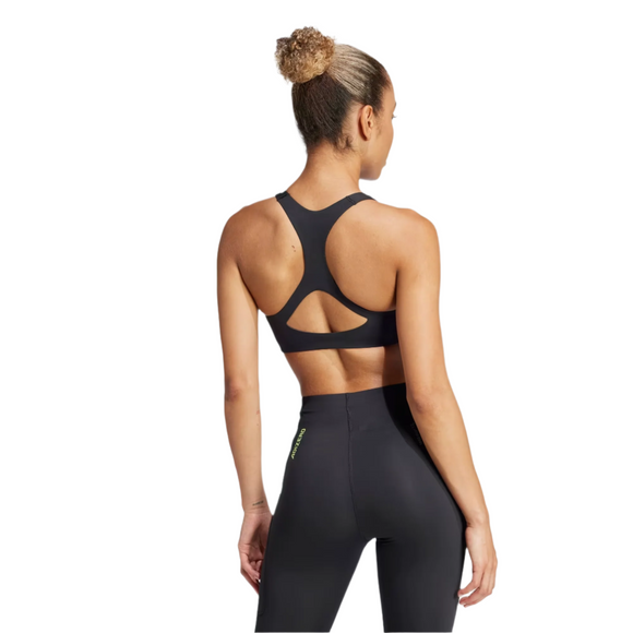 En kvinde med en krøllet knold ses bagfra iført den sorte Adidas Adizero Run Medium Support Bra til kvinder, parret med højtaljede leggings, på en almindelig hvid baggrund - klar til sin næste løbetur.