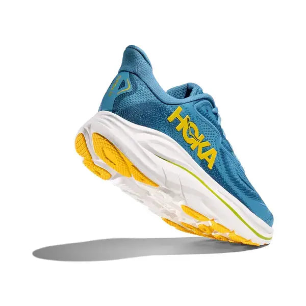 Hoka Clifton 10 Herre løbesko i Alpine Blue/Foggy Night vises mod en hvid baggrund og har støddæmpning, hvide såler samt gule og grønne detaljer, inkl. HOKA-logo på siden.