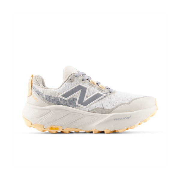 Et sidebillede af New Balance FreshFoam Hierro v9 Dame i Sea Salt/White Peach viser en lysegrå og hvid trailsko med meshdetaljer, en beige sål, gul slidbane og N-logoet på siden.
