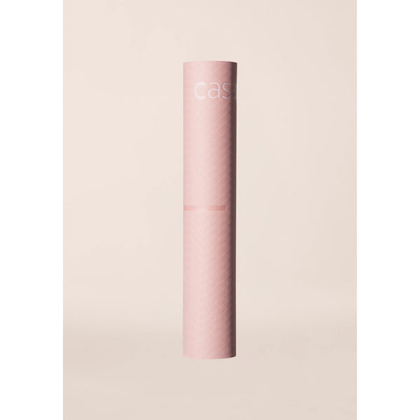 Et højt, cylindrisk, lyserødt rør med påskriften "Casall" står oprejst mod en lys beige baggrund og viser Yoga Mat Position 4mm, Unisex, i Light Pink/Pink.
