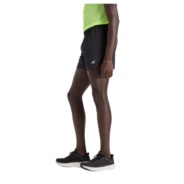 En person, der er synlig fra taljen og ned, er iført sorte New Balance RC Short 5" Herre shorts, en lysegrøn ærmeløs top og sorte løbesko på en almindelig hvid baggrund.