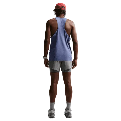En person står med front mod kameraet iført en rød kasket, Nike Nk Df Fast Singlet til mænd i Diffused Blue/Reflective Silver, grå shorts, grå sokker og grå sportssko på en almindelig hvid baggrund.