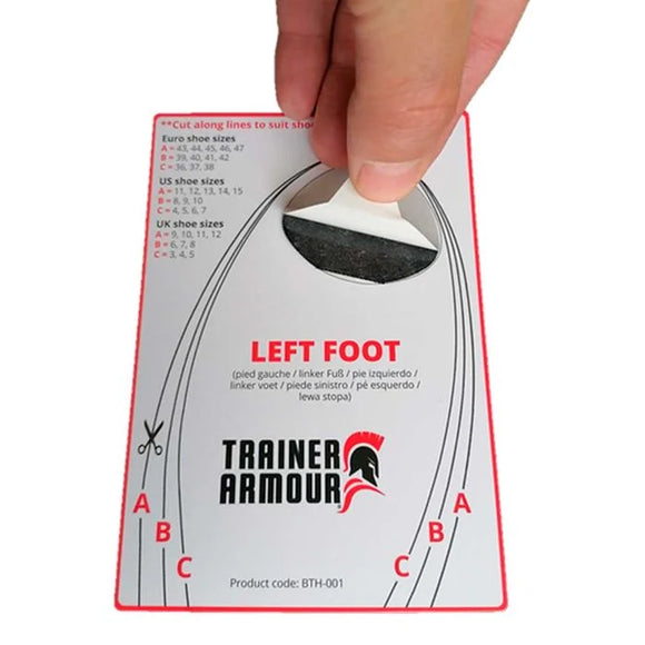 En hånd fjerner et klistermærke til venstre fod fra en Trainer Armour Big Toe Hole Preventer (Unisex, sort), som har størrelsesguider og skærelinjer A, B og C. Der er flersproget tekst på kortet.