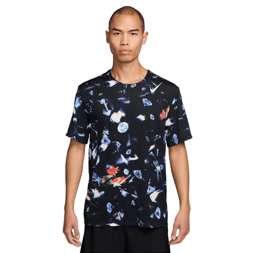 En person iført Nike Aeroswift Aop Ss Running T-Shirt til mænd i sort/laser orange står med front mod en almindelig lys baggrund.