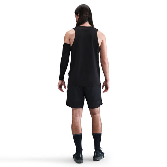 En person med langt mørkt hår kigger væk og er iført en Nike Dri-FIT Running Tank Top, Herre, Black/Reflective Silver, sammen med sorte shorts, sokker, sko og et sort ærme på venstre arm mod en almindelig hvid baggrund.