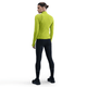En kvinde kigger væk iført en lysegrøn Nike Therma-FIT ADV 1/2-Zip Reflective Running Top (Cyber/Reflective Silv) med sorte, tætsiddende leggings og sneakers på en almindelig hvid baggrund.