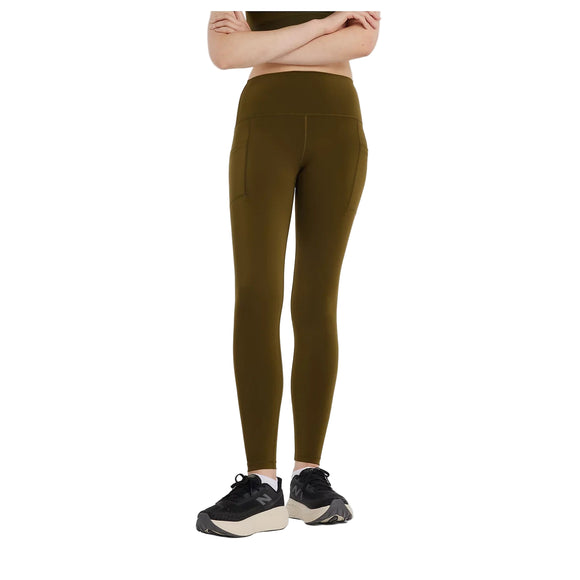 En person iført New Balance Sleek Pocket High Rise Legging, Dame, Woodland står med armene over kors og kigger fremad; vedkommendes sorte og hvide sportssko er synlige, men hovedet er ikke med på billedet.