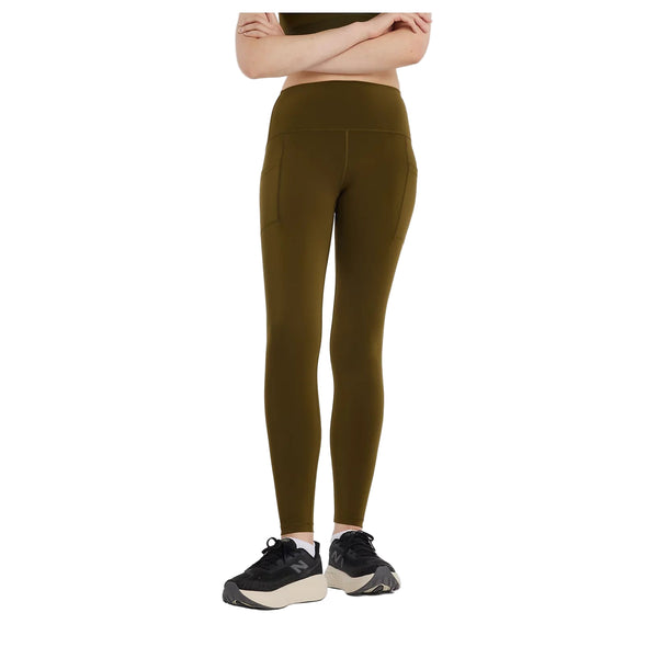 En person iført New Balance Sleek Pocket High Rise Legging, Dame, Woodland står med armene over kors og kigger fremad; vedkommendes sorte og hvide sportssko er synlige, men hovedet er ikke med på billedet.