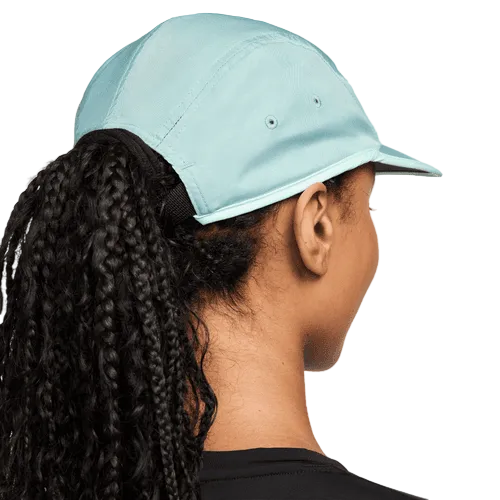 En person med langt, krøllet hår trukket gennem ryggen på en lyseblå Nike Fly Unstructured Swoosh Cap (Unisex, Cannon/Mint Foam/White), set bagfra i en sort skjorte. Kasketten har åndbart materiale, der giver komfort hele dagen.