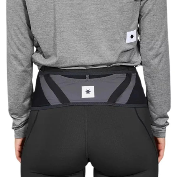 En person i grå langærmet skjorte og sorte sportsbukser ses bagfra iført et Saysky Flow Belt, Unisex, Black. Bæltet har et rektangulært mærke med en sort stjerne - ideelt til at bære løb-essentials sikkert.