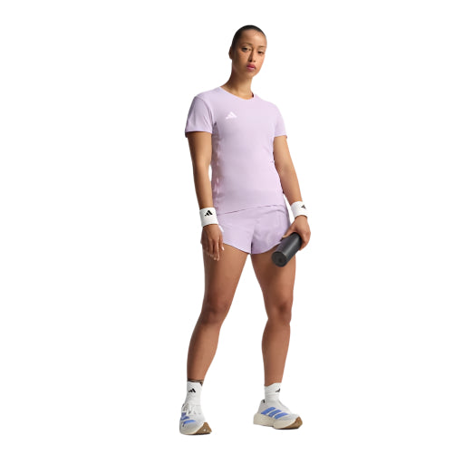 En kvinde bærer Adidas Adizero E Tee, Dame, Powplu i lyslilla og holder en tennisketcher. Hun kombinerer det med hvide armbånd, ankelstrømper og sneakers med blå detaljer på en almindelig hvid baggrund.