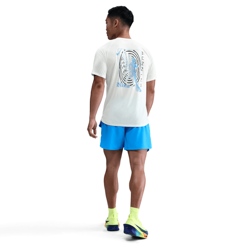 En person står med ryggen til og er iført Nike Stride Running Short-Sleeve Top i Sail, lyseblå shorts, gule sokker og farverige sneakers på en almindelig hvid baggrund.