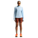 En person kigger fremad i en Nike ACG Half Zip Running Top, Dame, Hydrogen Blue/Summit White, rustne Adidas-shorts, orange løbesko, brune sokker og reflekterende sportssolbriller på en hvid baggrund.