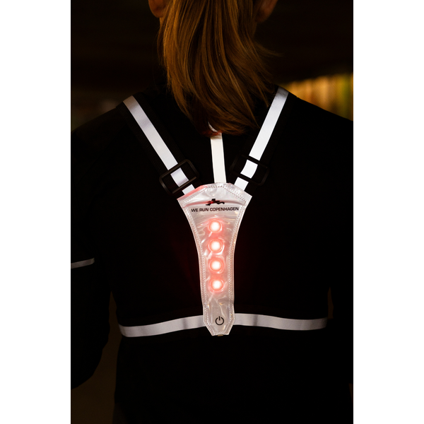 En person bærer en BeeSafe LED Harness USB Phone Pocket, Unisex, Silver, med reflekterende stropper og fire røde lysdioder på ryggen. "WE RUN COPENHAGEN" er trykt i nærheden af lysene - ideelt til løb om natten.