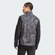 En mand kigger væk fra kameraet iført Adidas Otr Sd Vest M til mænd i Grefou/Black med ensfarvede sorte ærmer og sorte bukser på en almindelig lys baggrund.