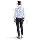 En person står med ryggen til kameraet iført en lys jakke med hætte, Nike Dri-FIT Mid-Rise løbebukser til kvinder i sort/reflekterende sølv og sportssko på en almindelig hvid baggrund.