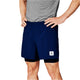 En person iført en grå t-shirt og blå Saysky Pace 2in1 Shorts 5" til mænd med et hvidt rektangulært logo på venstre ben står med hænderne på hofterne mod en hvid baggrund - ideel til trailløb.