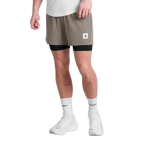 En maratonløbers nederste halvdel ses på en hvid baggrund iført Saysky Pace 2 in 1 Shorts 5'', Herre, Taupe med sorte liners, en hvid t-shirt, strømper og sneakers.