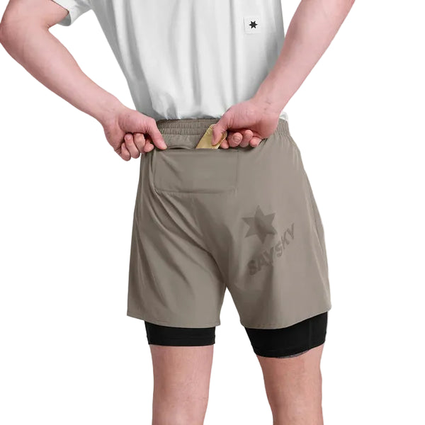 En person ses bagfra lægge en solbrun genstand i den bageste lynlåslomme på Saysky Pace 2 in 1 Shorts 5'', Herre, Taupe, med et sort inderlag og stjernelogo - perfekt til maratonløbere.
