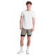 En person smiler mod en hvid baggrund iført en hvid t-shirt, Saysky Pace 2 in 1 Shorts 5'' Herre i Taupe, hvide sokker og sneakers. Med kort, krøllet hår er dette look ideelt til maratonløbere, der ønsker komfort og stil.