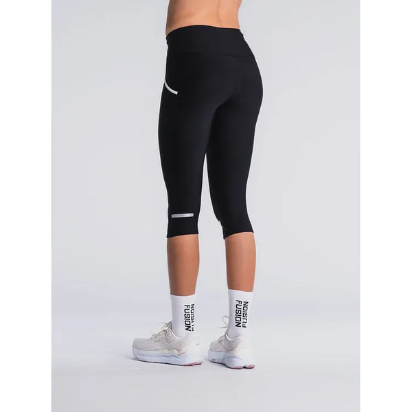 En person kigger væk og er iført Fusion 3/4 Tights Unisex i SuperBlack, hvide sokker med NOOSA FUSION-tekst og hvide løbesko på en almindelig lys baggrund.