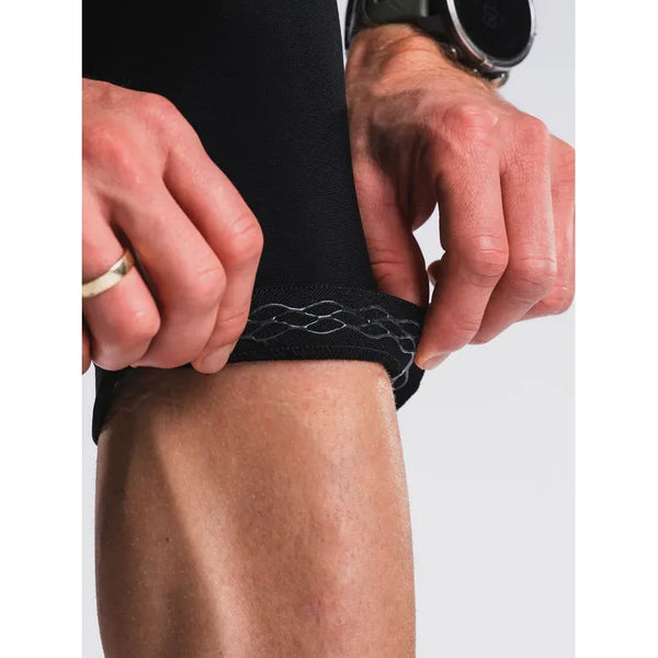 Et nærbillede viser hænder, der justerer kanten på Fusion 3/4 Tights, Unisex, SuperBlack, og afslører et silikonegreb. Personen bærer en ring og et mørkt armbåndsur, som fremhæver disse premium træningstights fra Fusion.