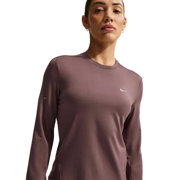 En kvinde i Nike Swift UV Long Sleeve Shirt, Dame, Tattoo/Reflective Silv står på en hvid baggrund. Den lilla skjorte har et lille hvidt Nike-logo på brystet og giver UV-beskyttelse til aktive dage udendørs.