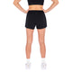 En kvinde kigger væk fra kameraet, klædt i en sort sports-bh og Fusion Run Shorts, Dame, Black, sammen med hvide sokker og sneakers på en hvid baggrund.