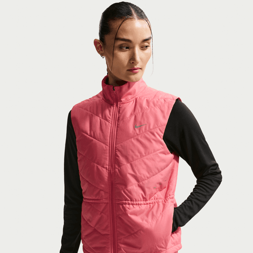 En kvinde med mørkt hår, der er bundet tilbage, bærer Nike Swift Running Vest til kvinder i Sea Coral/Reflective Silver over en langærmet sort skjorte og kigger lidt til venstre mod en almindelig lys baggrund.