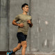 En mand iført en LiiteGuard Ground-Tech T-shirt til mænd i farven Dusty Green jogger udendørs foran en stor betonmur.