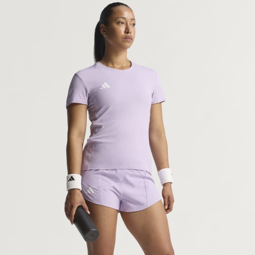 En kvinde er iført Adidas Adizero E Tee, Dame, Powplu - en lyslilla løbetrøje - med hvide armbånd og holder en sort vandflaske. Hun står på en almindelig hvid baggrund og kigger lidt til siden.