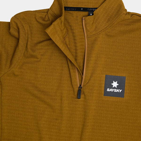 Blaze Half Zip Light Fleece til kvinder fra Saysky kommer i camel med en sort lynlås og et brystmærke med en hvid stjerne og SAYSKY-logo. Kraveetiketten viser mærkets navn og størrelse S - perfekt som et let, teknisk mellemlag.